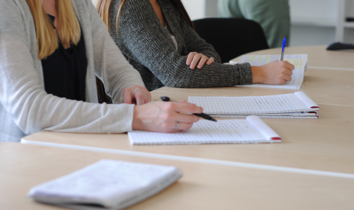 Group of students writing notes at a meeting in a well-lit classroom.