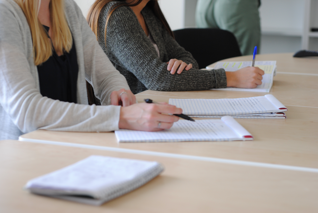 Group of students writing notes at a meeting in a well-lit classroom.